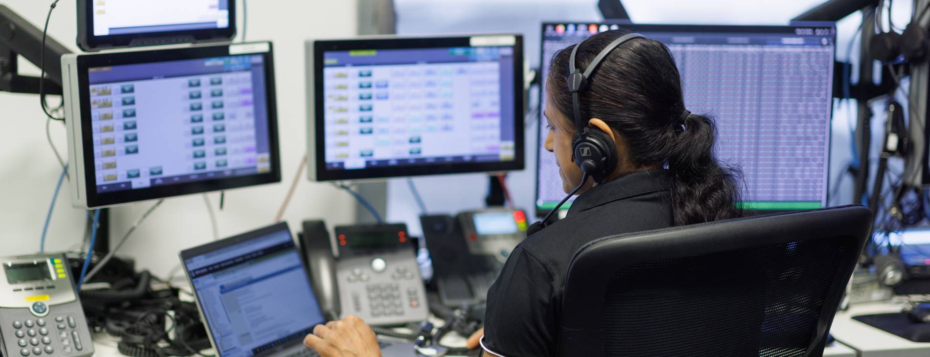 a femal controller wearing a headset infront of five screens and several phones